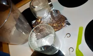 Szklanka, folia aluminiowa, sól, łyżeczka i kolczyki na blacie.