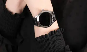 Damski smartwatch z czarnym paskiem na nadgarstku, na tle czarnej bluzki.