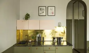 Nowoczesna kuchnia z zielonymi szafkami i błyszczącym panelem ściennym imitującym złoto w płatkach. Dwie grafiki nad szafkami dodają charakteru.