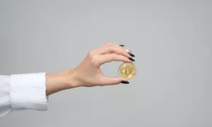 Dłoń z czarnym lakierem trzyma złotą monetę z symbolem Bitcoina. Zastanawiasz się, ile kosztuje złota moneta?