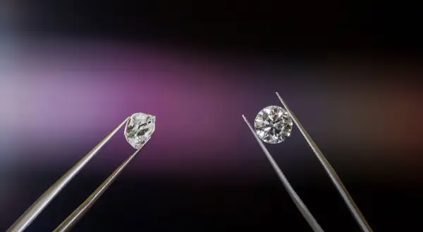 Dwa kamienie szlachetne w pęsecie: surowy brylant i oszlifowany diament.