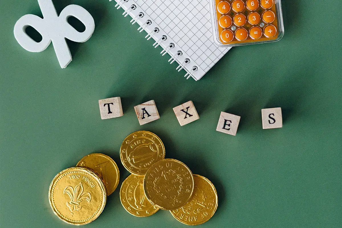 Złote monety, kalkulator i kostki z napisem "TAXES" sugerują rozważania o zakupie złota a podatek PCC.