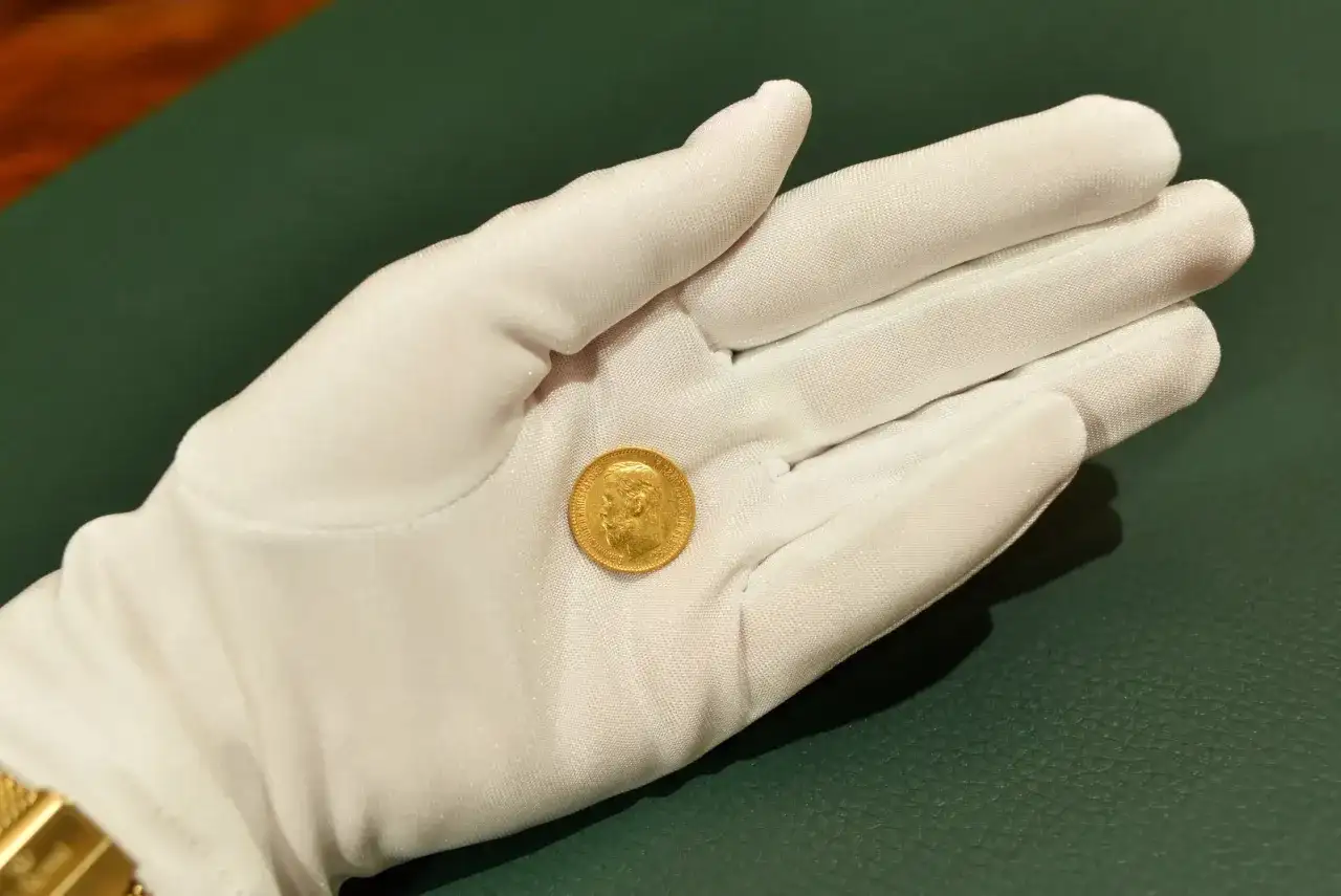 Złota moneta 5 rubli 1898, prezentowana na białej rękawiczce, błyszczy niczym skarb z przeszłości.