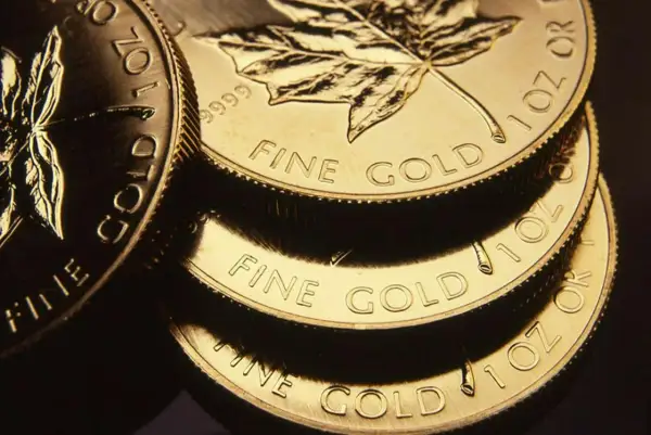 Stos złotych monet z liściem klonu i napisem "FINE GOLD".